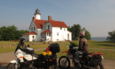 2 motorcycles parked in front of a lighthouse with water in the distance